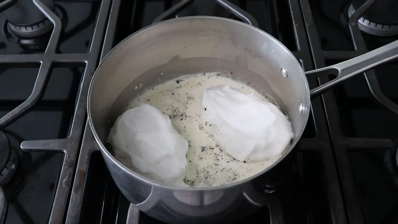 two poached meringue islands in a saucepan with vanilla-specked milk