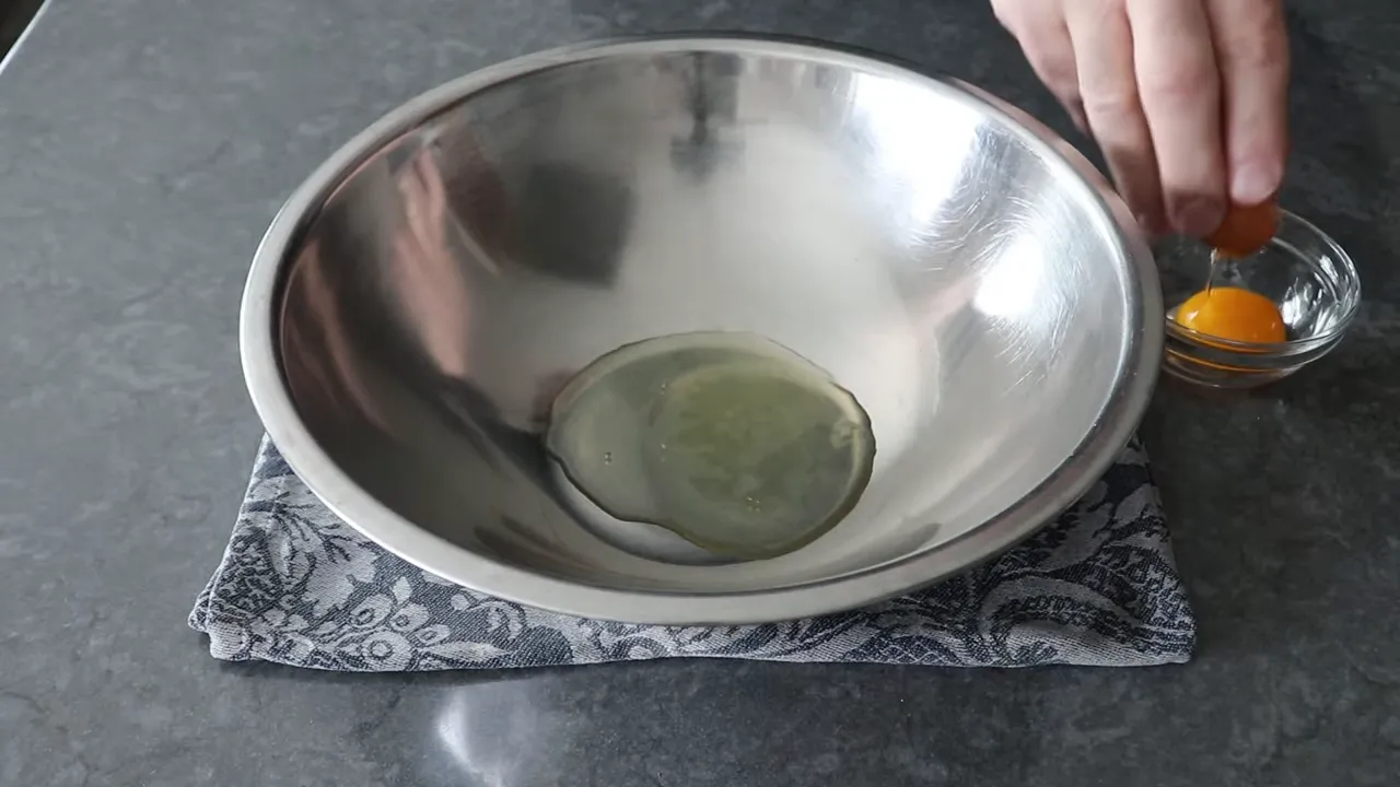 Separated egg white in a stainless steel mixing bowl and yolk in a small glass bowl