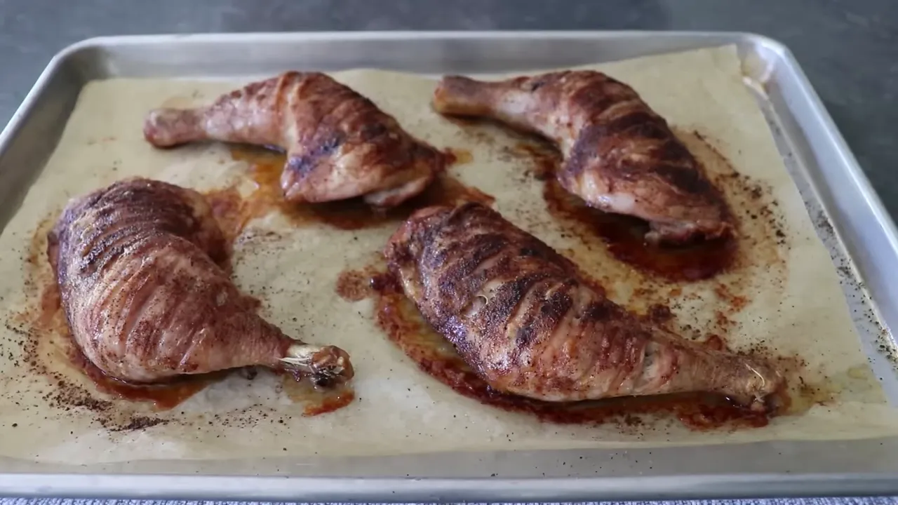 Four roasted chicken leg quarters with tiger cuts showing browned, crispy skin on a parchment-lined sheet pan