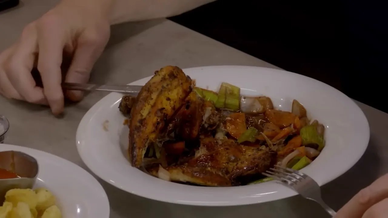 roasted chicken with root vegetables on a white plate being carved