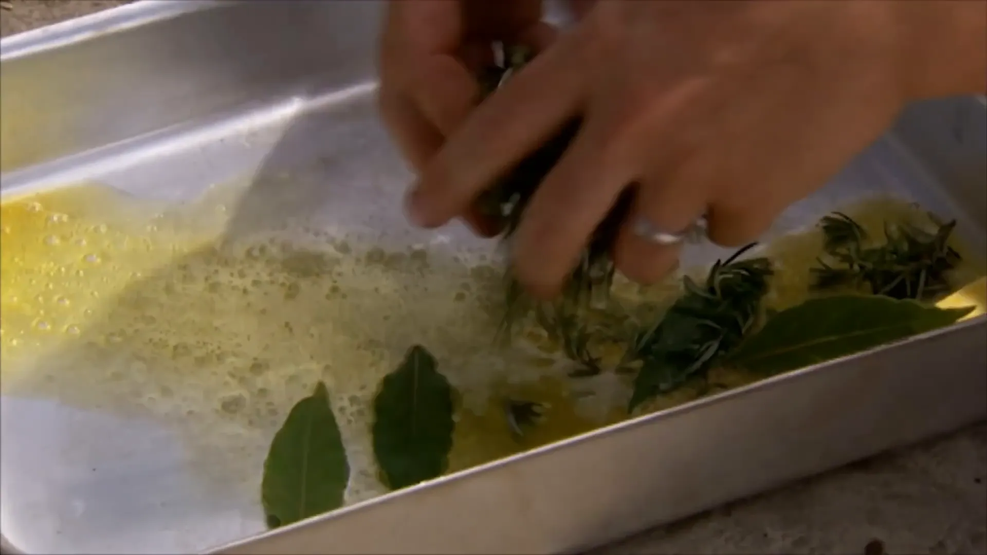 Butter, olive oil, bay leaves, and rosemary heating in a roasting tray