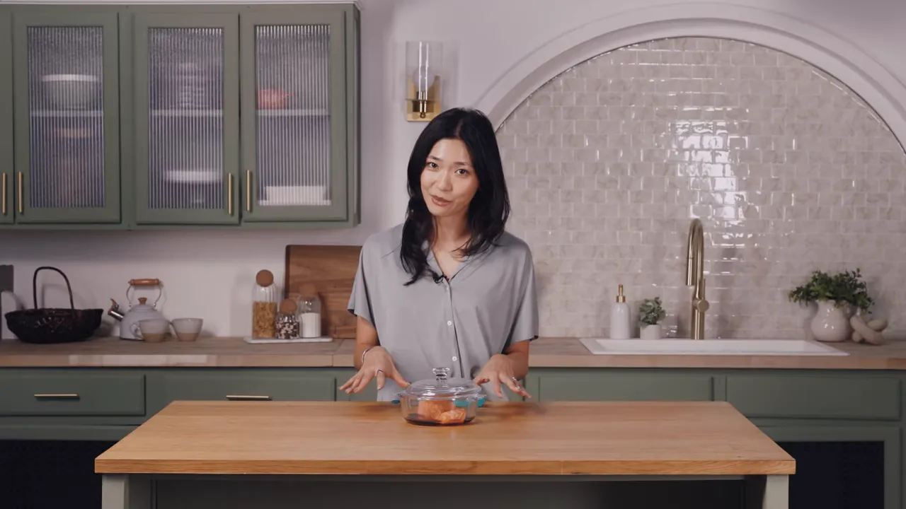 Presenter standing behind a kitchen island with a covered glass dish holding a salmon fillet, set up and ready to cook.