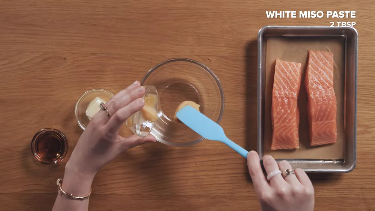 Top-down view of mixing miso butter in a bowl with two raw salmon fillets on a tray