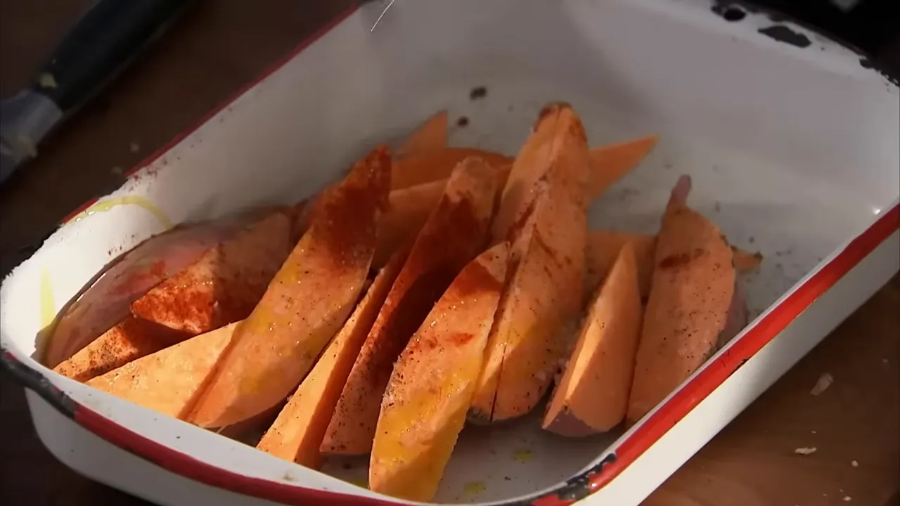Seasoned sweet potato wedges arranged in an enamel roasting tray with oil and paprika
