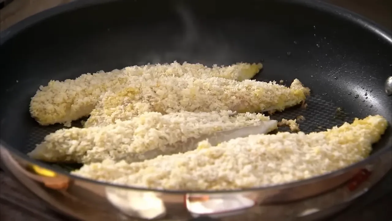 Close-up of breadcrumb-coated pouting fish fingers frying in a skillet