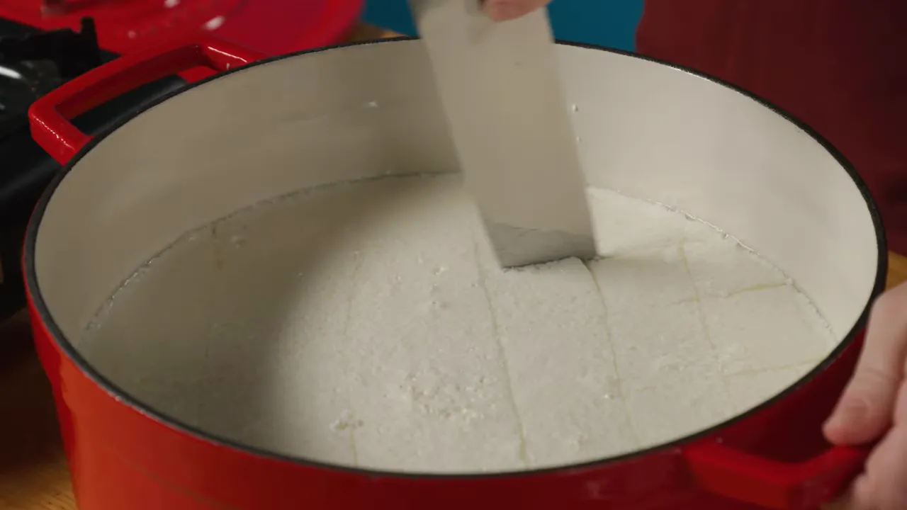 cutting mozzarella curds into squares in a red pot