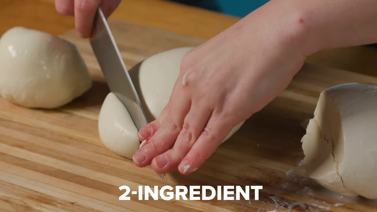 Close-up of hands slicing a ball of fresh mozzarella on a wooden board with a '2-INGREDIENT' overlay