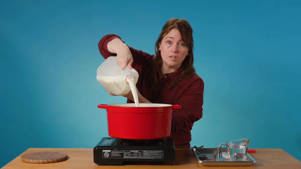 Person pouring a gallon of milk into a red pot on a portable burner with measuring tools at the side