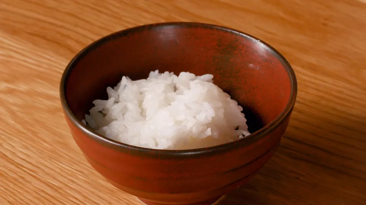 Steaming white short‑grain rice served in a small brown ceramic rice bowl on a wooden table.