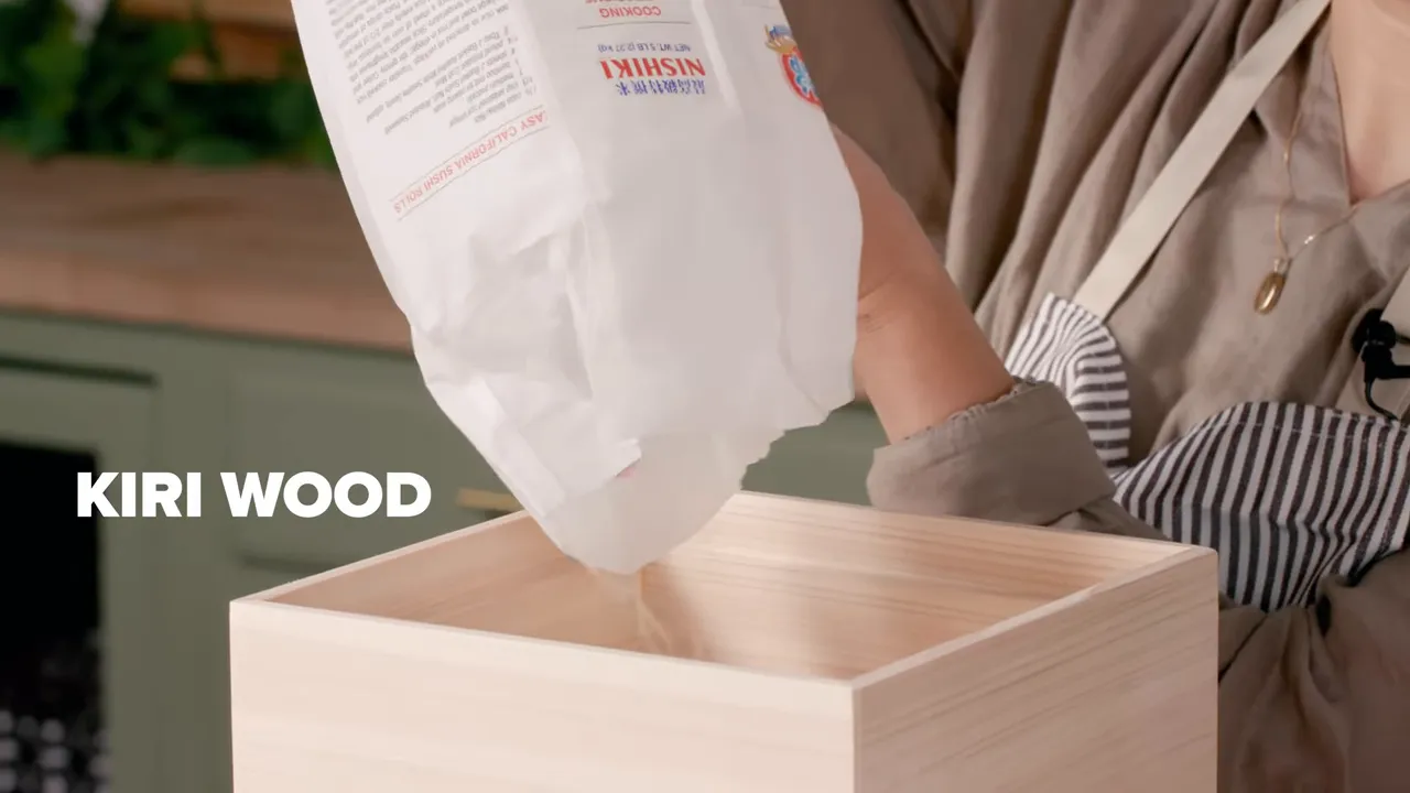 Rice being poured from a bag into a wooden kiri storage box with on-screen label 'KIRI WOOD'