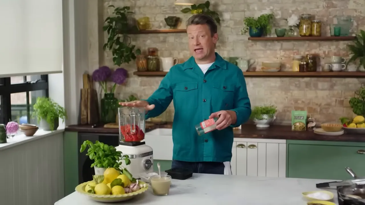 blender on counter filled with roasted red peppers and basil while cook gestures