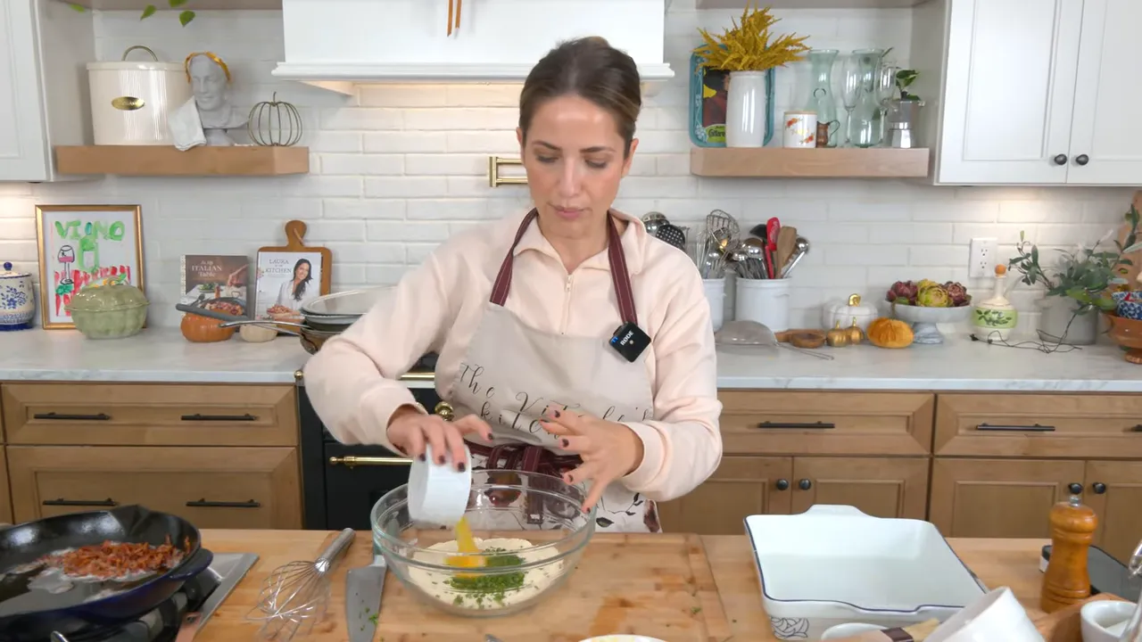 Cook pouring beaten egg from a white ramekin into a glass bowl containing dry cornbread mix and chopped scallions on wooden board