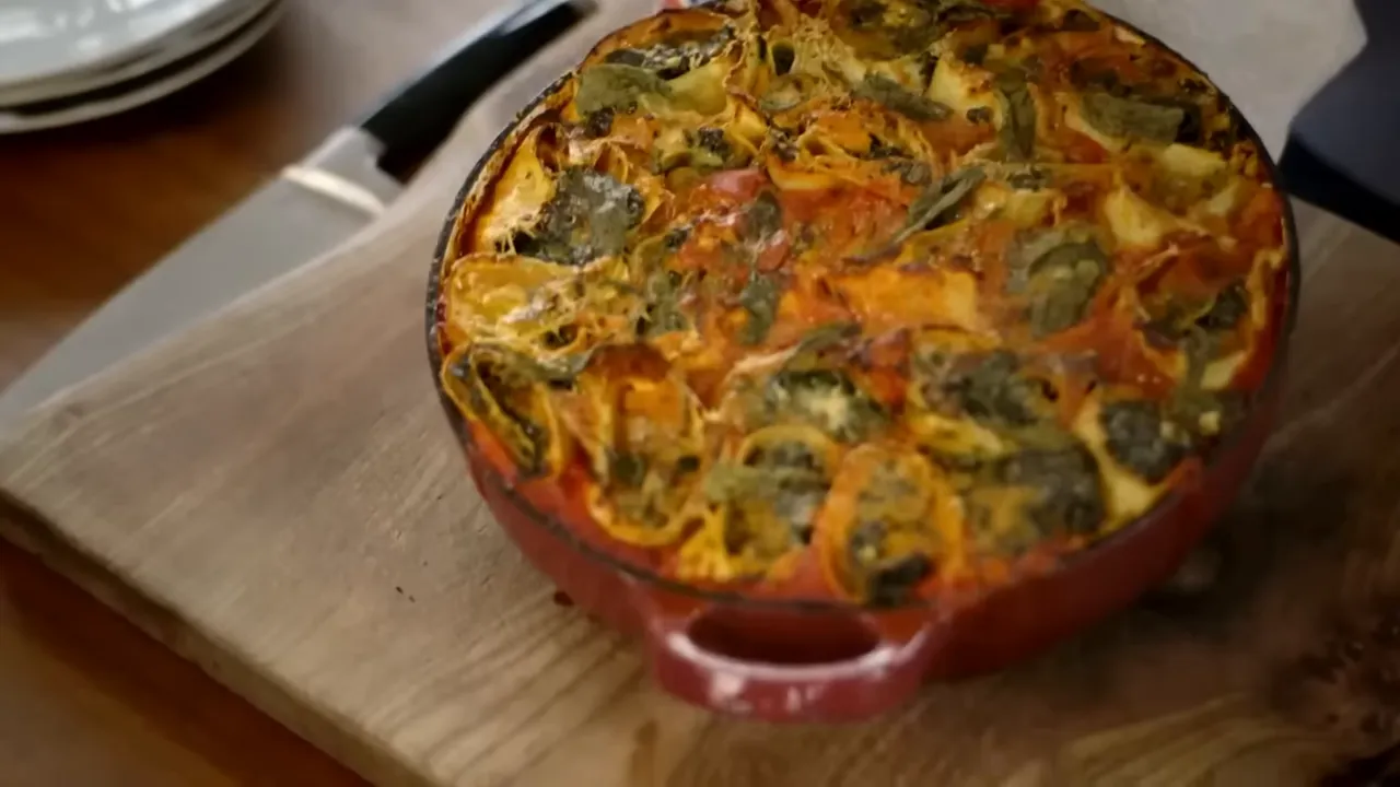 Top-down view of finished squash and spinach rotolo in a red baking dish on a wooden board, showing spiral parcels and melted cheese