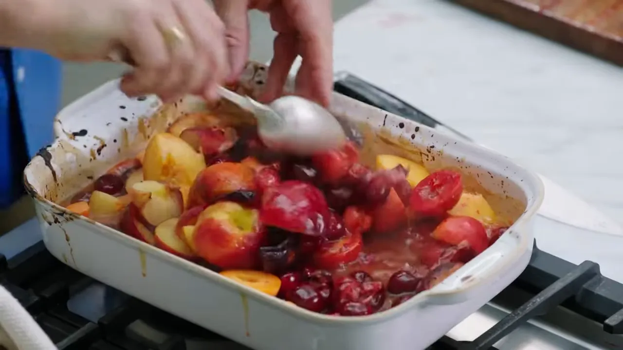 Spoon pouring the orange and strawberry sauce over mixed stone fruit