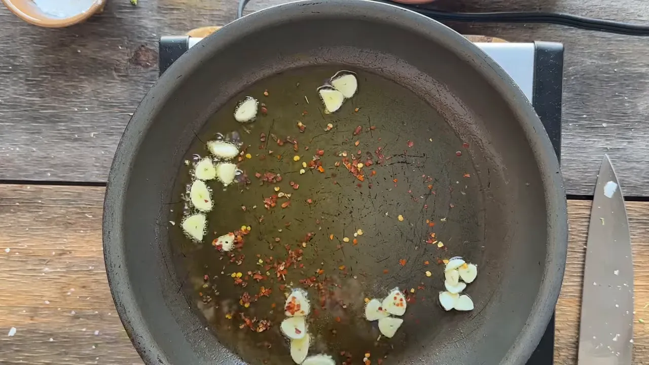Overhead skillet with garlic slices and red pepper flakes sizzling in olive oil