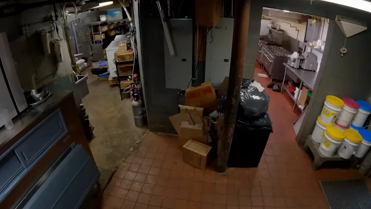 Cluttered restaurant back hallway with cardboard boxes and a garbage bag obstructing the walk-in entrance.