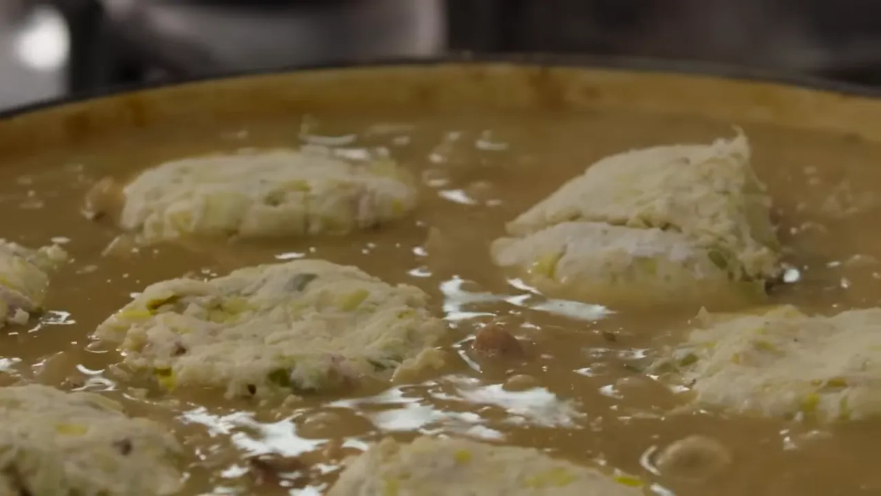 Close-up of several biscuit dumplings poaching in a rich turkey gravy in a wide pan