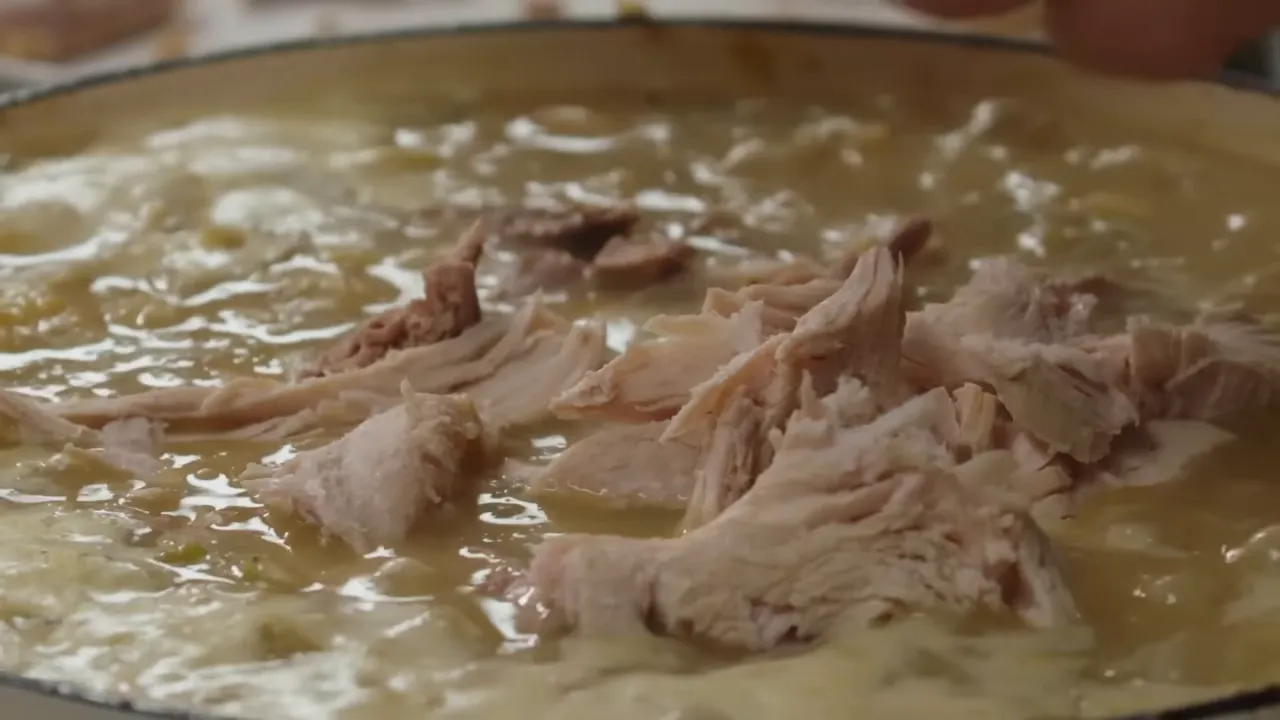 Shredded turkey pieces resting on top of a thick, glossy stew in a shallow pan