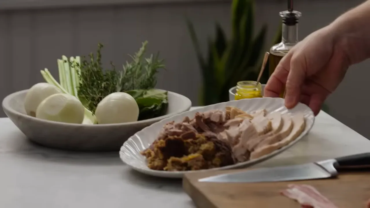 plate of sliced leftover turkey and a scoop of stuffing beside onions and fresh herbs on a kitchen counter