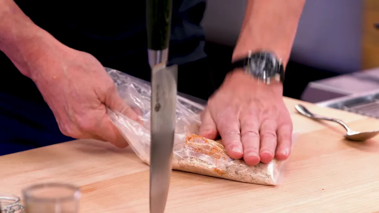 Hands pressing and flattening seasoned breadcrumbs inside a plastic bag on a cutting board
