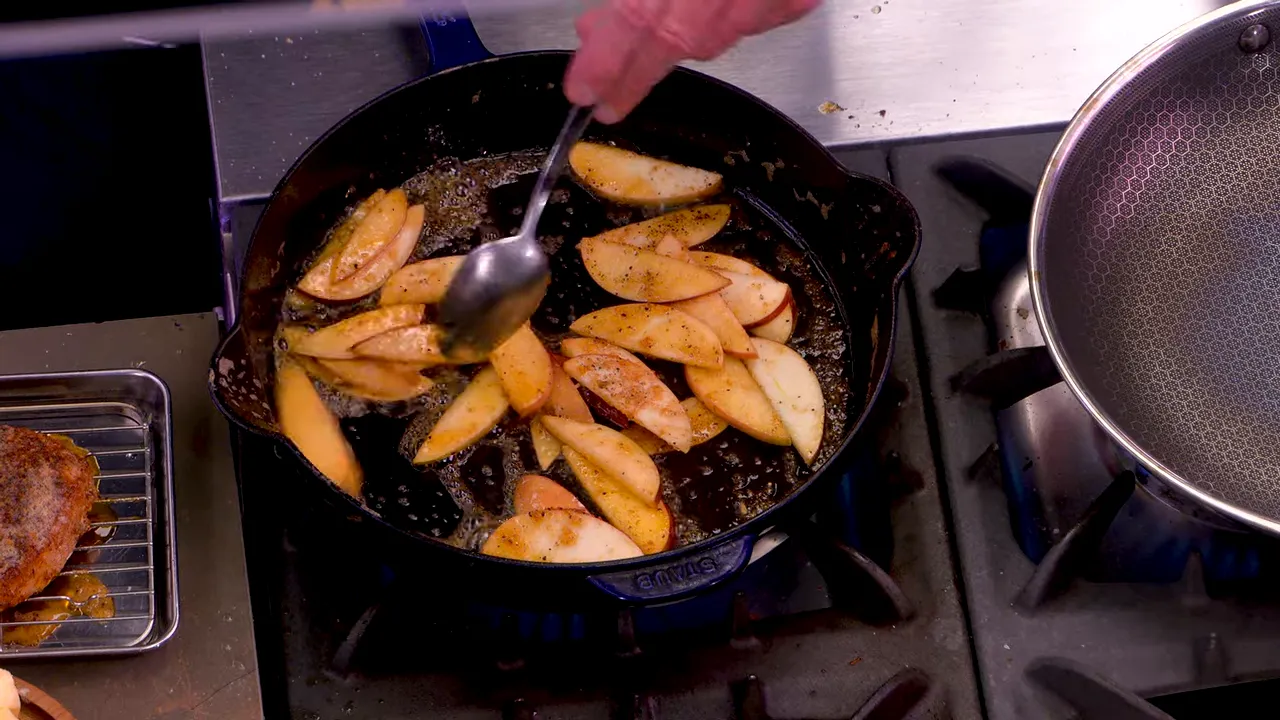 Spoon basting caramelized apple slices in a cast-iron skillet with pan juices