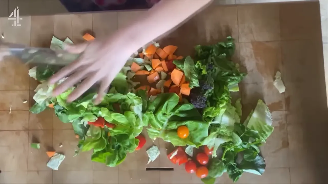 overhead view of bite-sized chopped salad ingredients on a wooden board with a hand arranging them