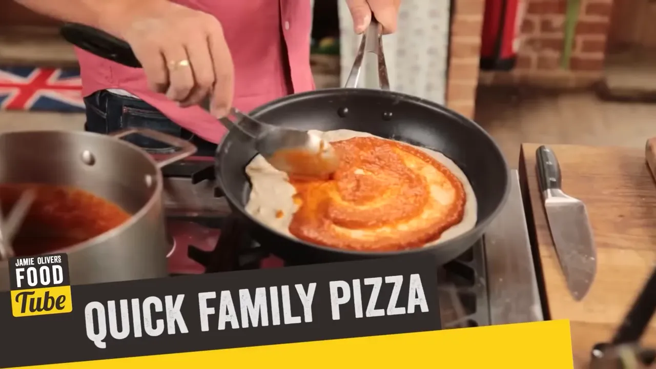spoon spreading tomato sauce on a pizza base in a frying pan