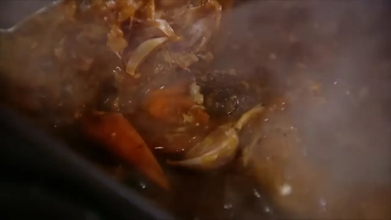 Roasted carrots, garlic cloves and giblets simmering in roasting tray juices with steam