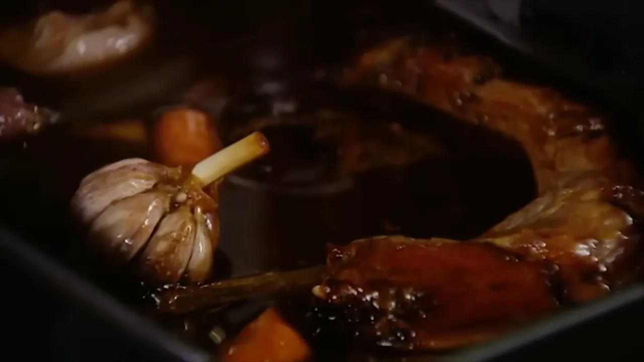 Roasting tray with a whole garlic bulb, carrot pieces and a pool of dark concentrated gravy.
