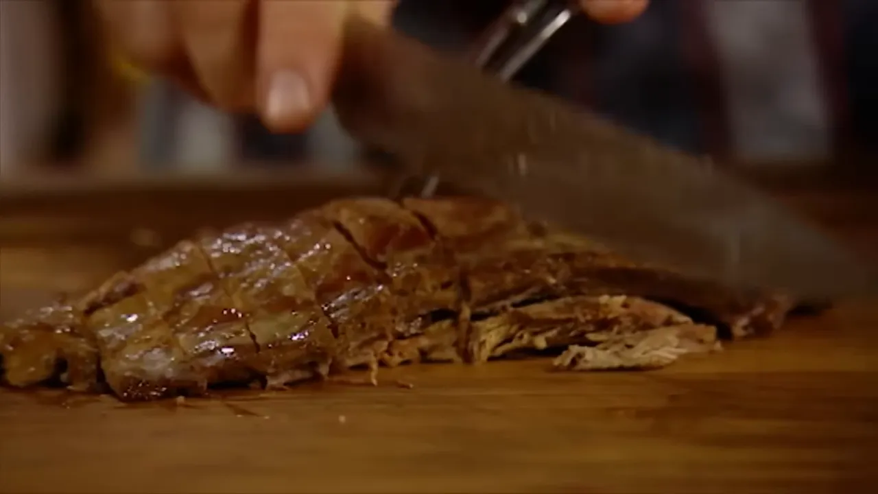Roast meat sliced on a wooden board being carved with a large knife