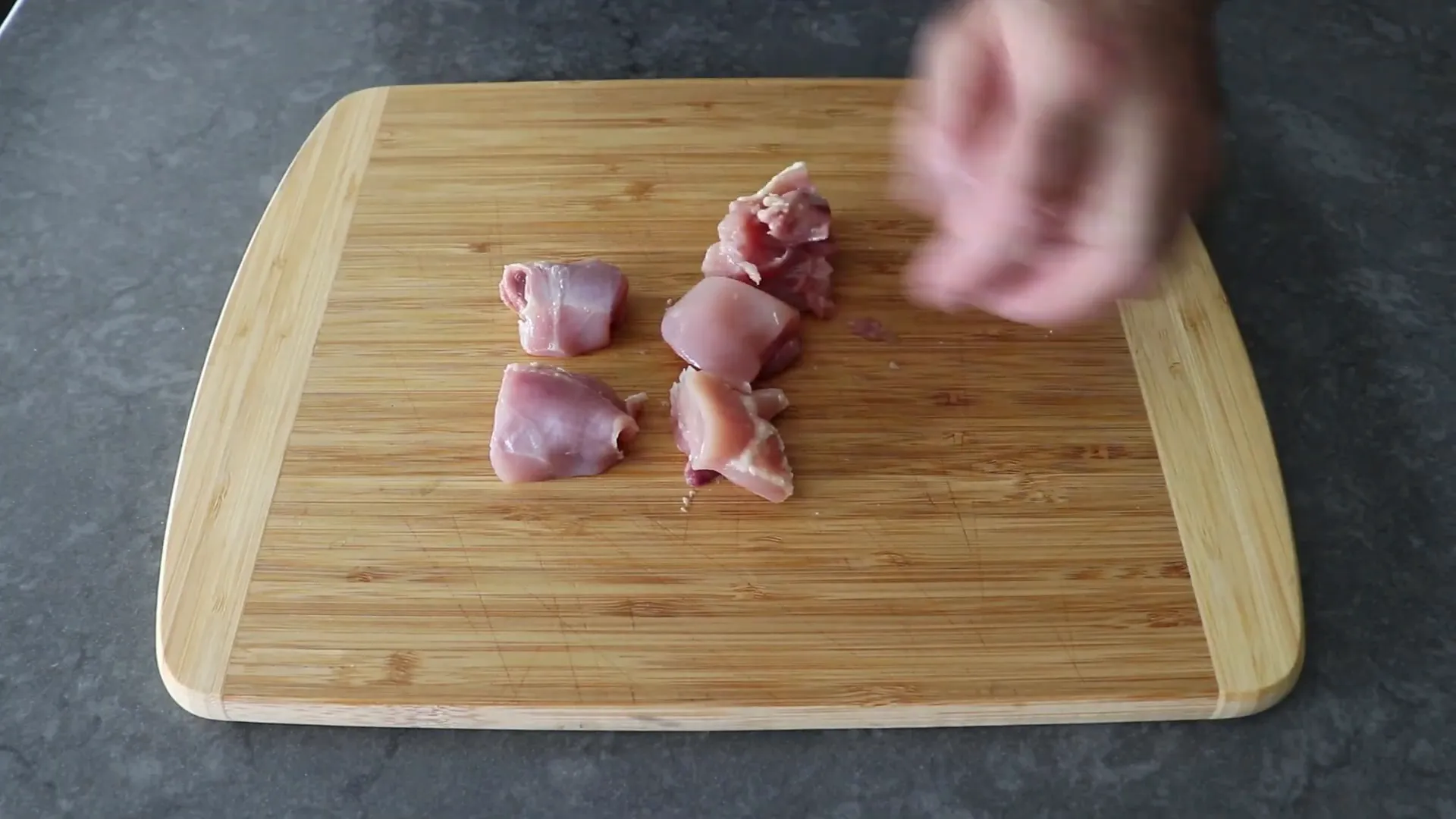 Cutting boneless chicken thighs into chunks for satay