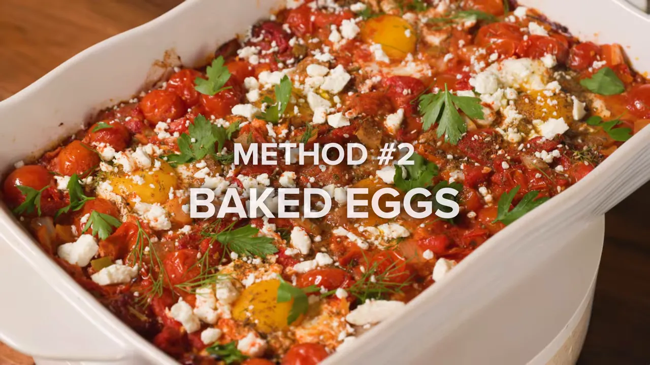 White baking dish filled with baked shakshuka: blistered cherry tomatoes, peppers, eggs, feta and herbs