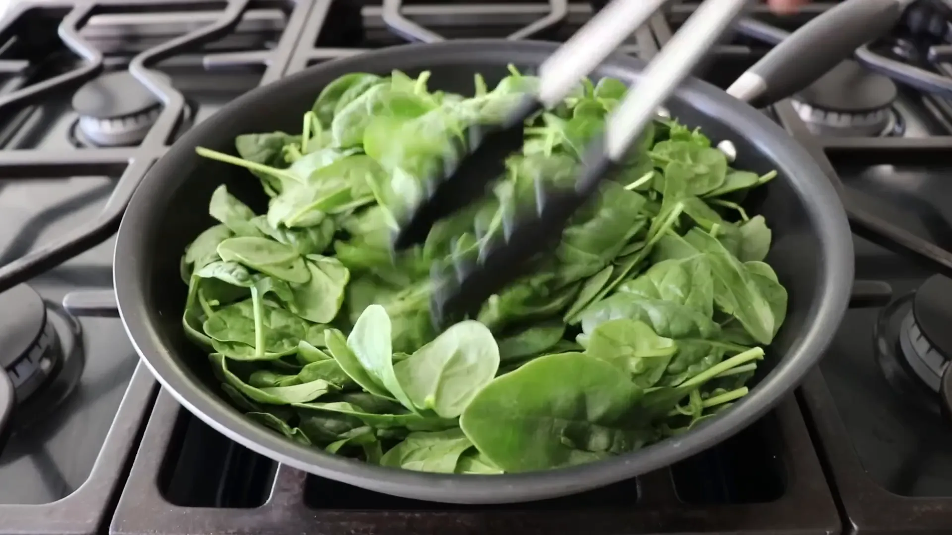 Fresh spinach wilting in skillet with olive oil