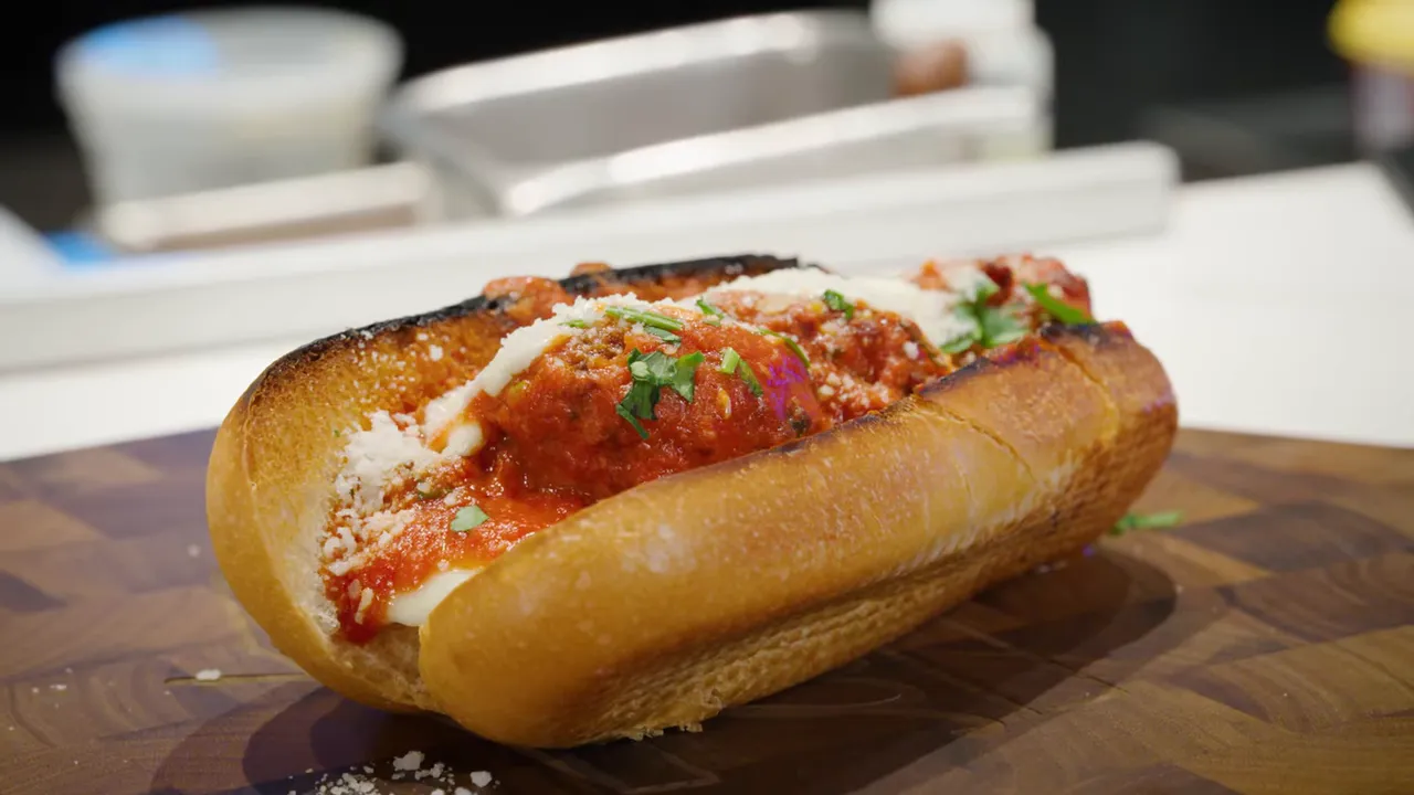 Close-up of a toasted meatball sub with melted cheese, marinara and fresh herbs on a wooden board