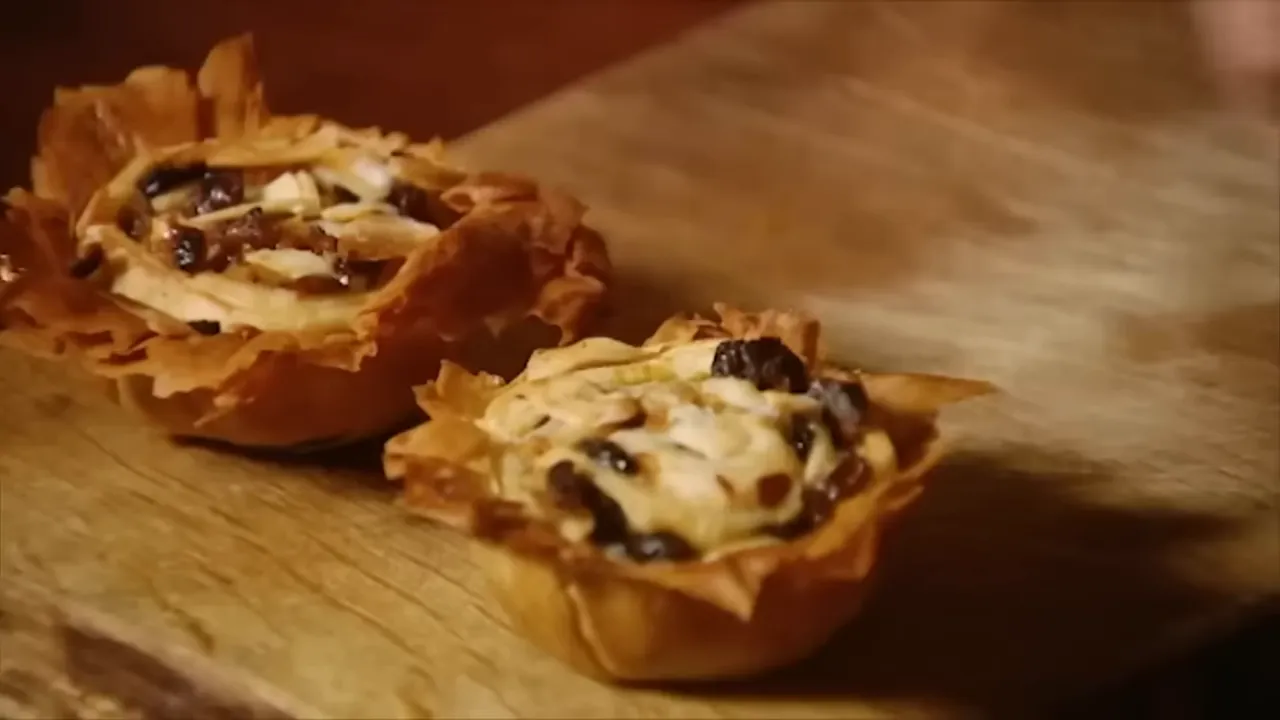Two golden filo mince pies on a wooden board, topped with sliced almonds and cranberries