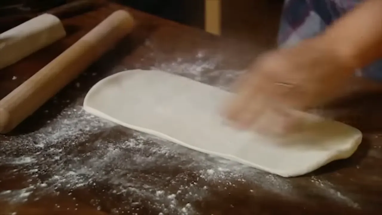 close-up of rolling pin flattening puff pastry on a floured board