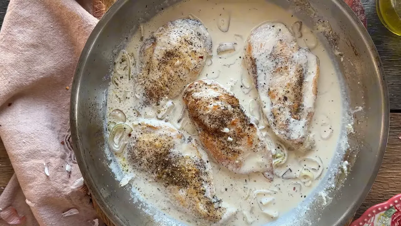 Seared chicken breasts simmering in a thick, creamy sauce with sliced shallots and visible pepper flecks