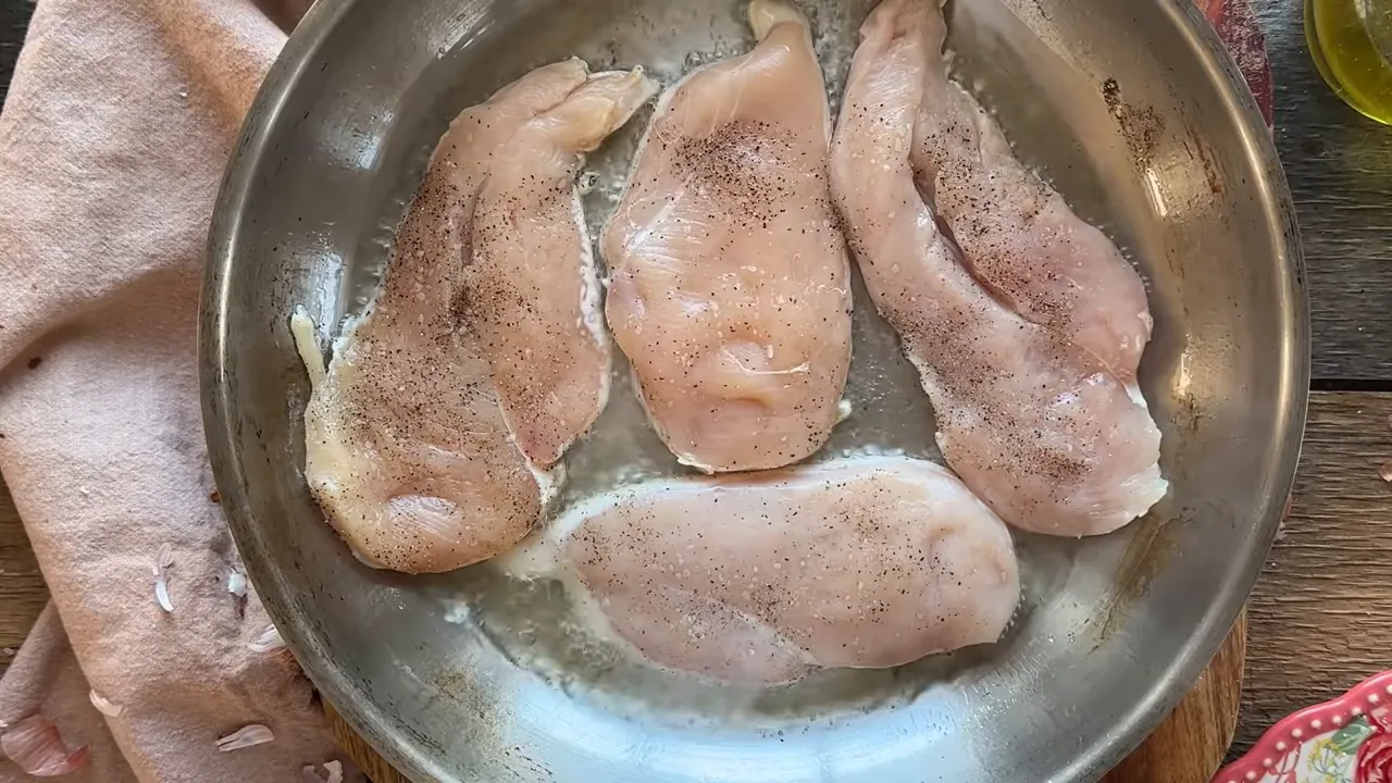 Four seasoned chicken breasts spaced in a stainless-steel skillet forming a sear