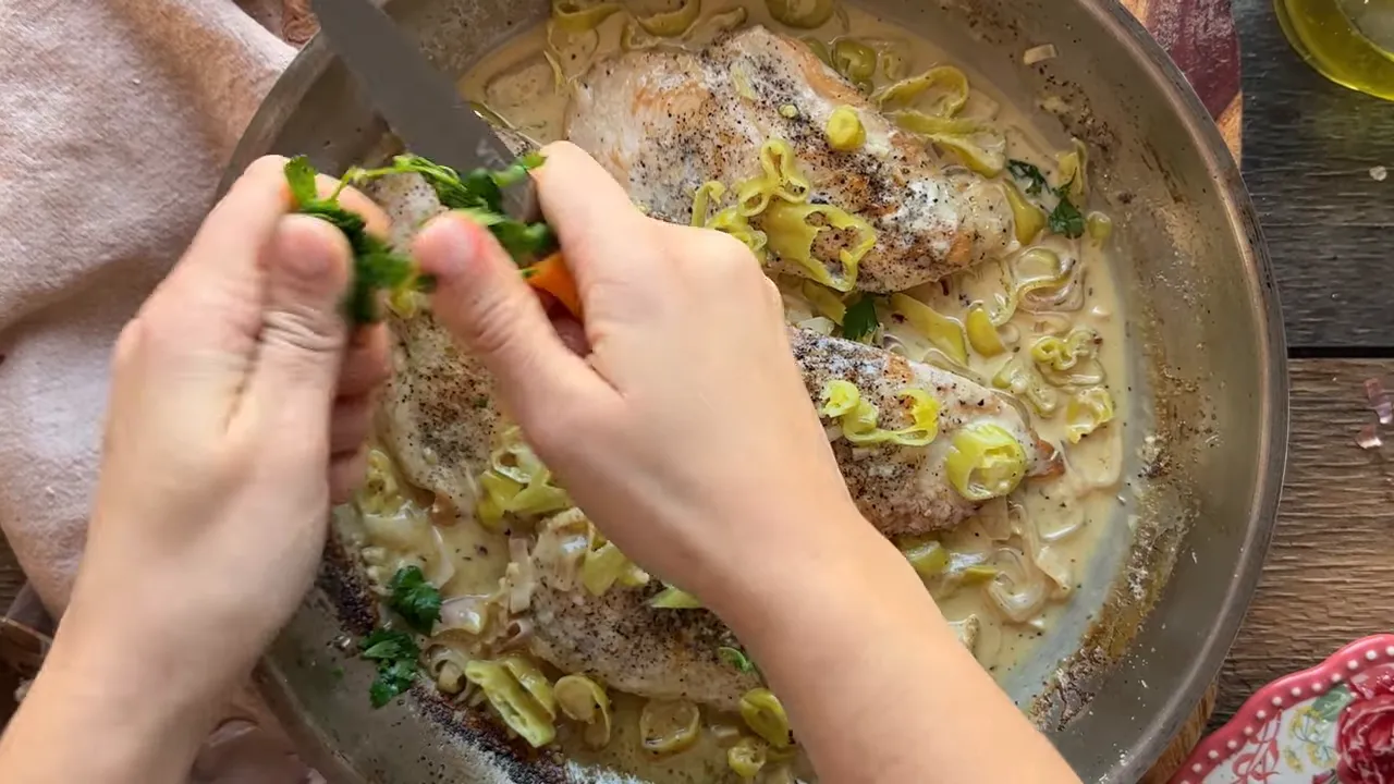 Hands tearing fresh parsley over a skillet of seared chicken in a creamy peperoncini sauce