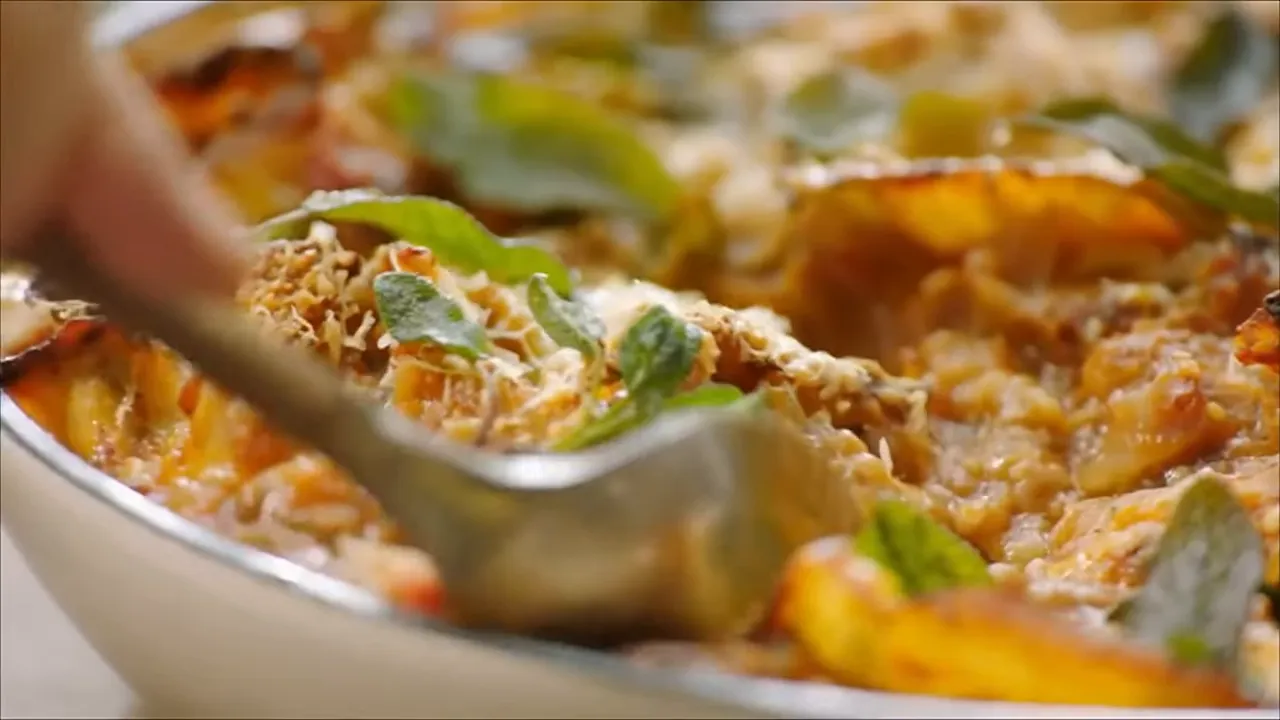 Close-up of baked aubergine lasagne showing golden cheese, crushed almonds and sage leaves being served with a spoon