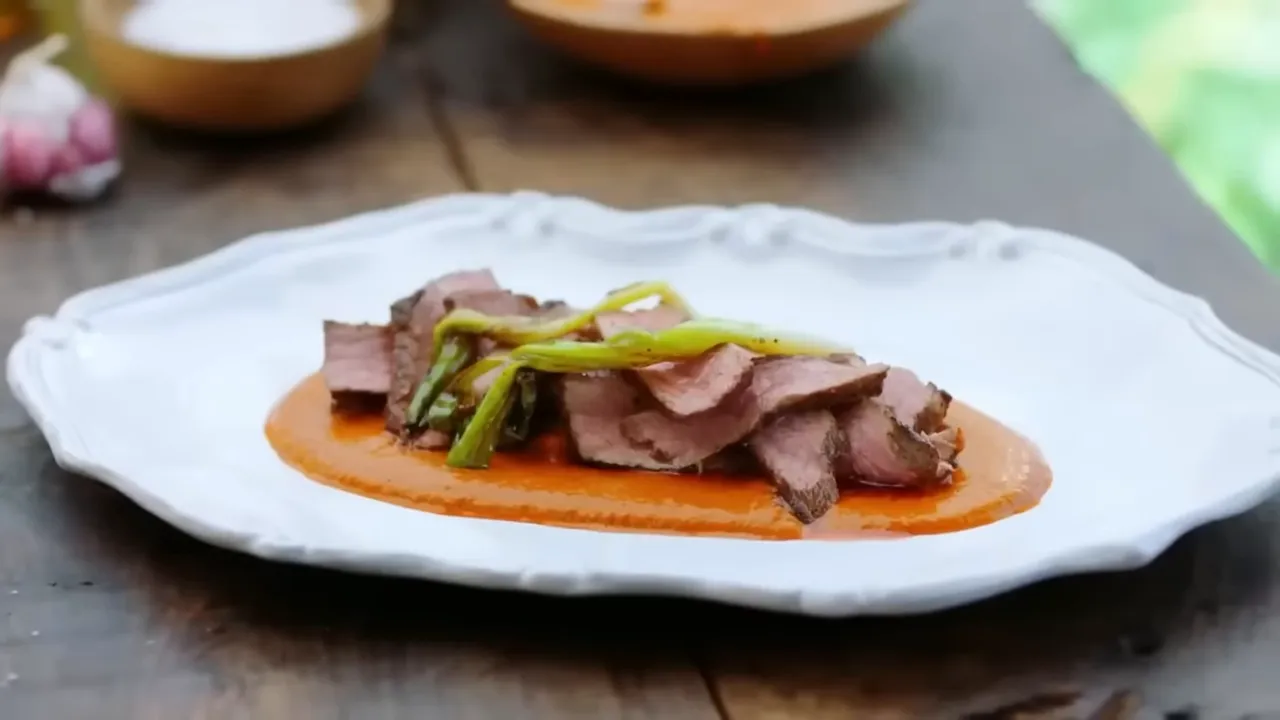Plated sliced sirloin served on a red chimichurri sauce with charred spring onions