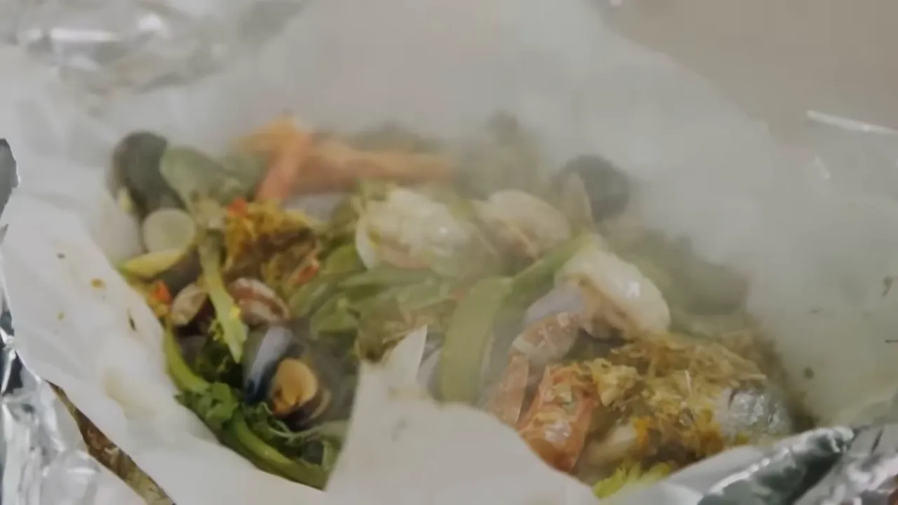 Open parchment and foil parcel showing mussels, prawns and Asian greens with steam