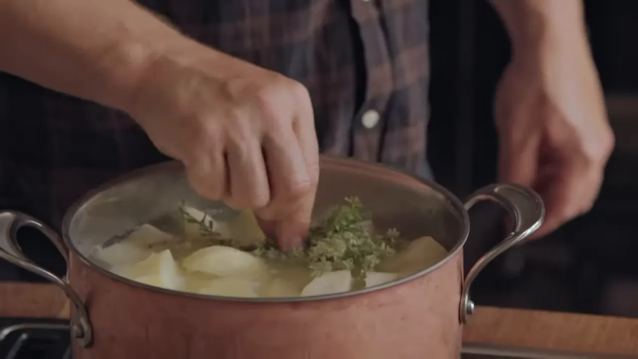 adding a thyme bundle into a pot of potato and celeriac chunks cooking in water
