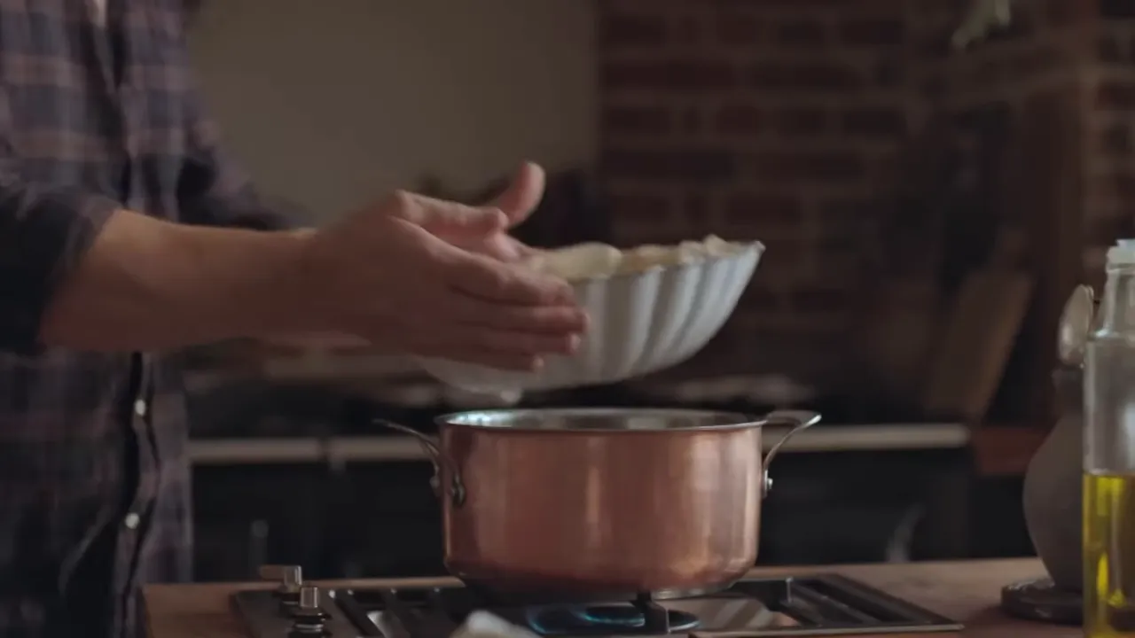 Chef placing a fluted serving bowl onto a copper pot to steam and keep mashed potatoes warm