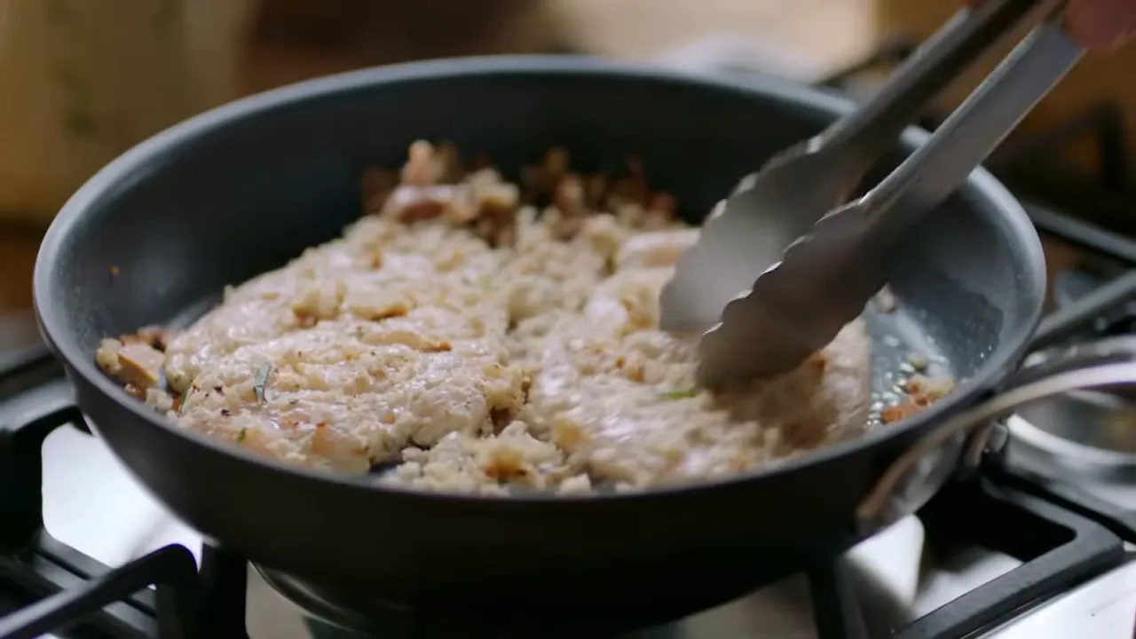 Breadcrumb-coated chicken breasts being pressed with tongs in a frying pan