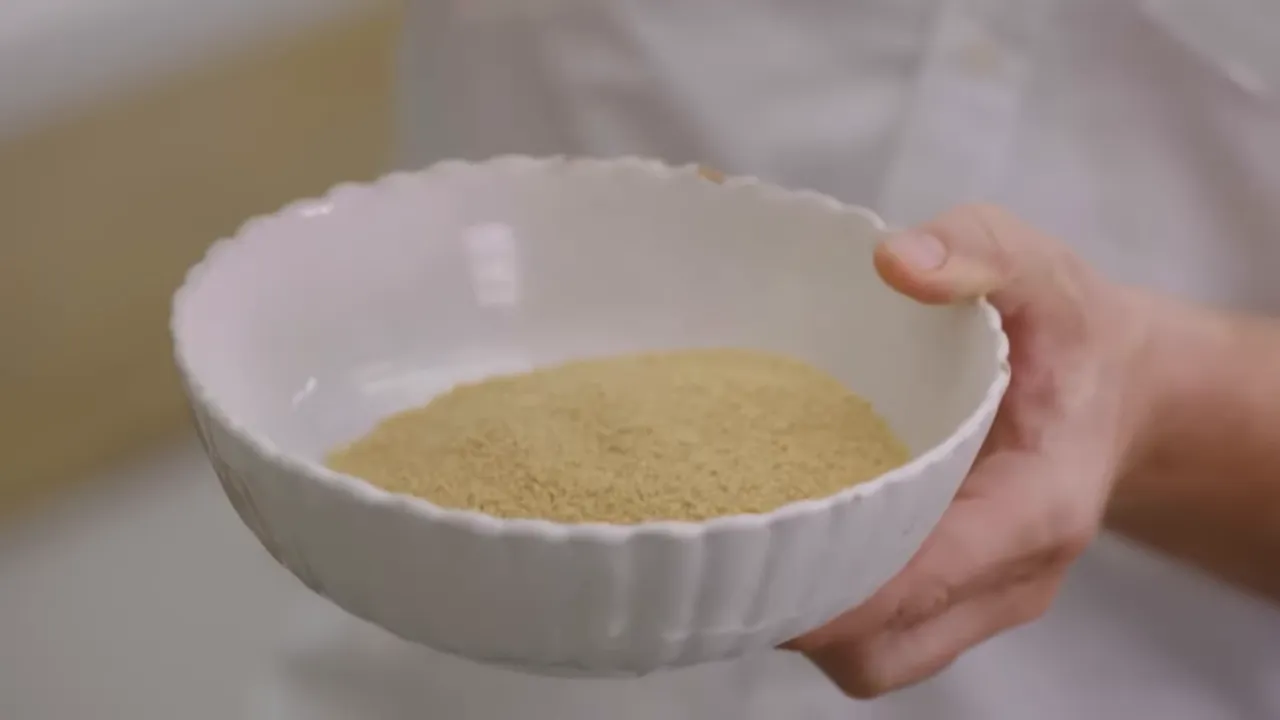 White bowl held in hand containing dry wholewheat couscous