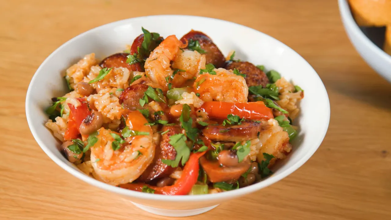 Plated bowl of one‑pot jambalaya with shrimp, andouille sausage, red peppers and chopped parsley on a wooden table