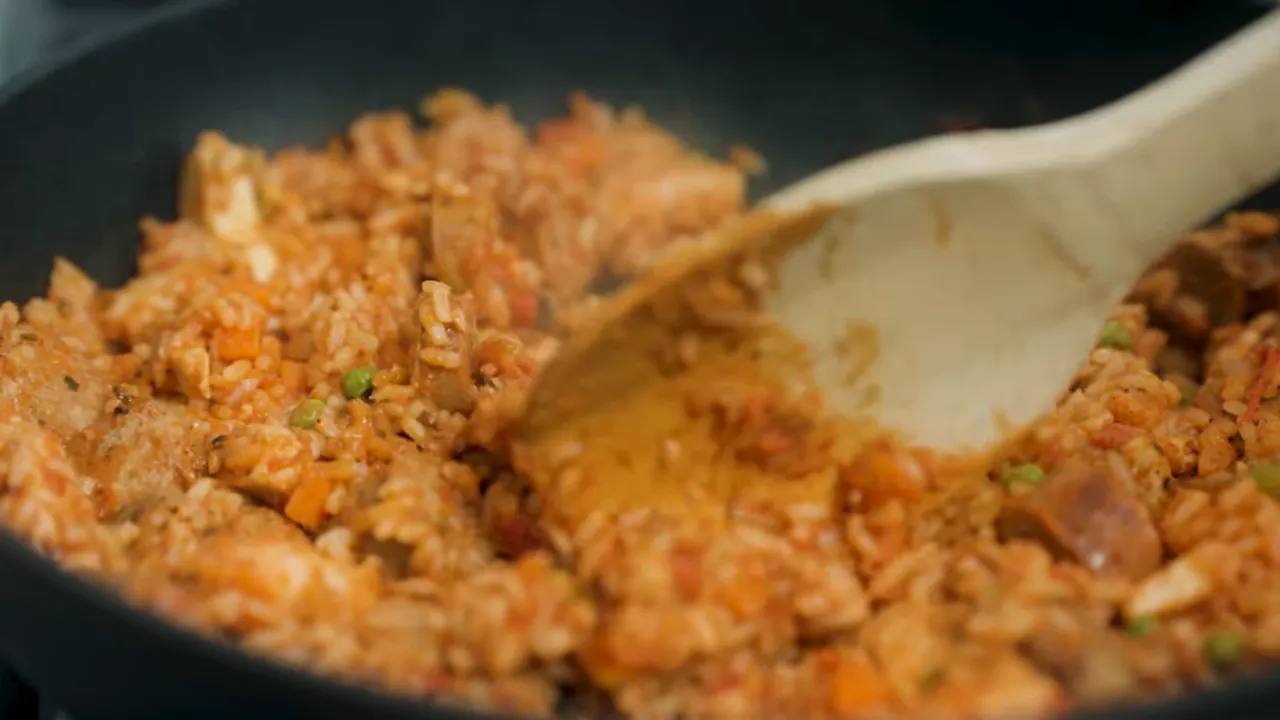 wooden spoon stirring finished one-pot jambalaya with rice, shrimp and sausage