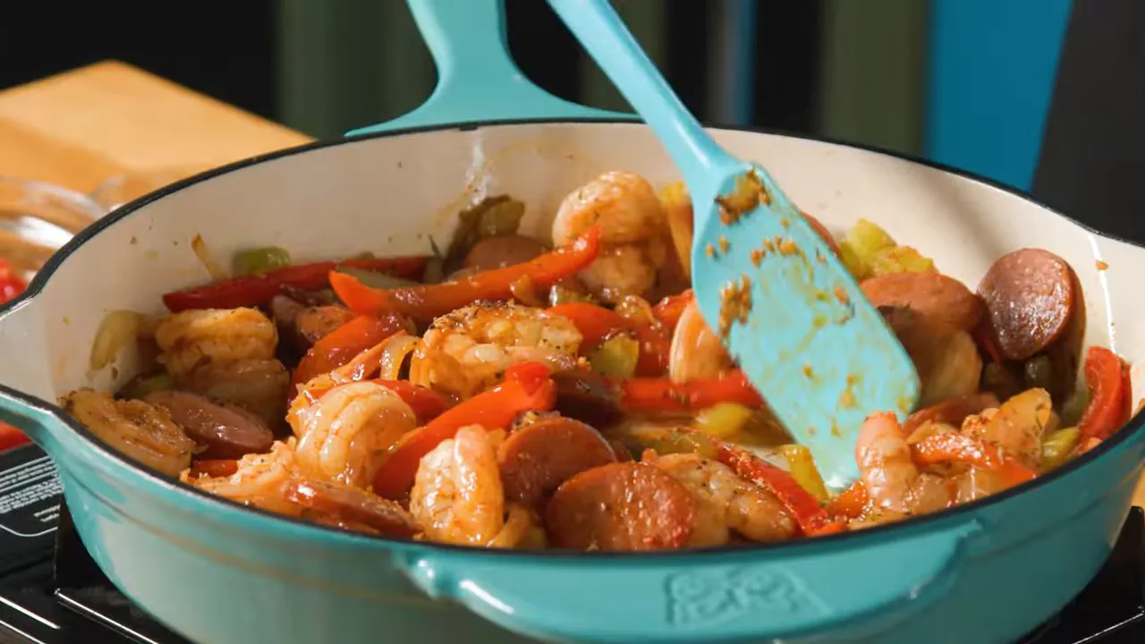 Close-up of jambalaya in a turquoise Dutch oven showing shrimp, andouille sausage, red peppers and a turquoise spatula.