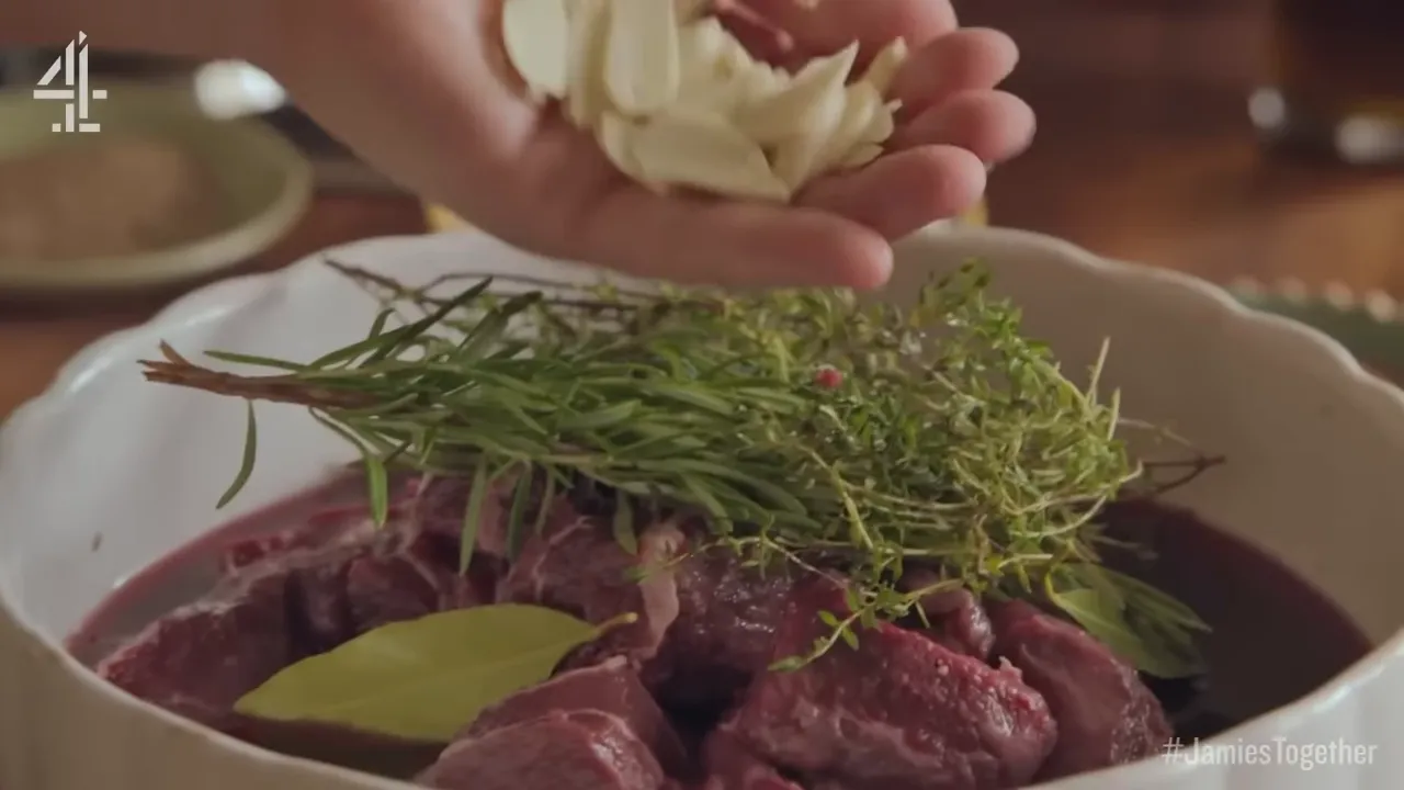 Hand sprinkling sliced garlic and placing rosemary and thyme over beef in a wine marinade
